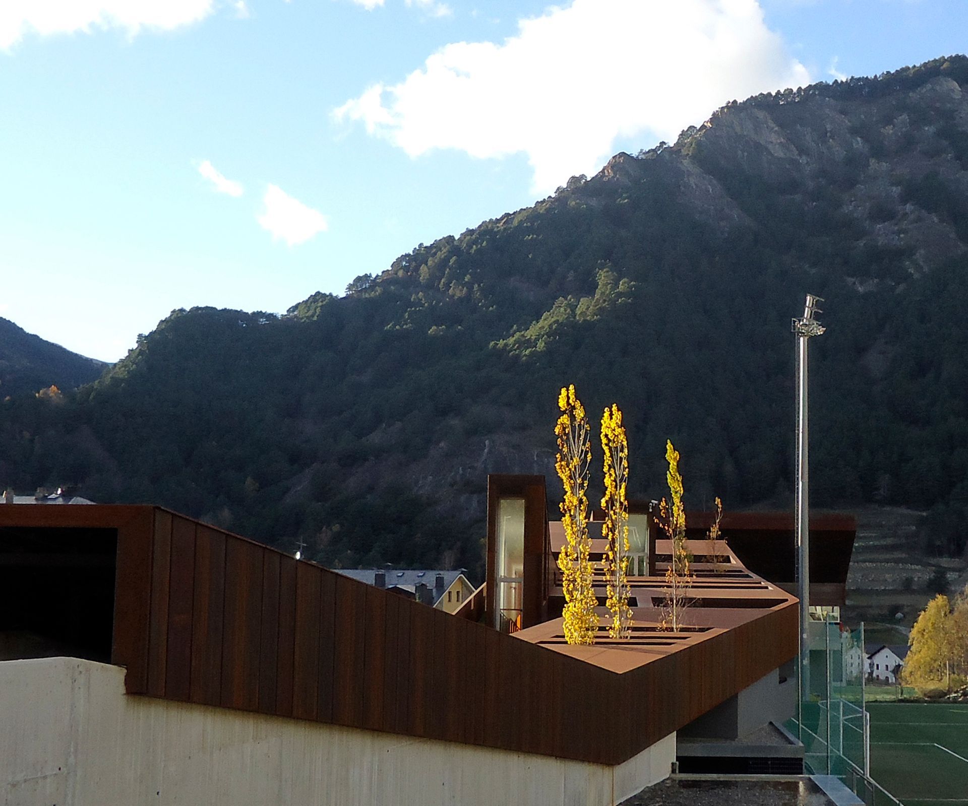 Teulades de pobles de muntanya amb una terrassa de fusta i arbres grocs contra un vessant boscós