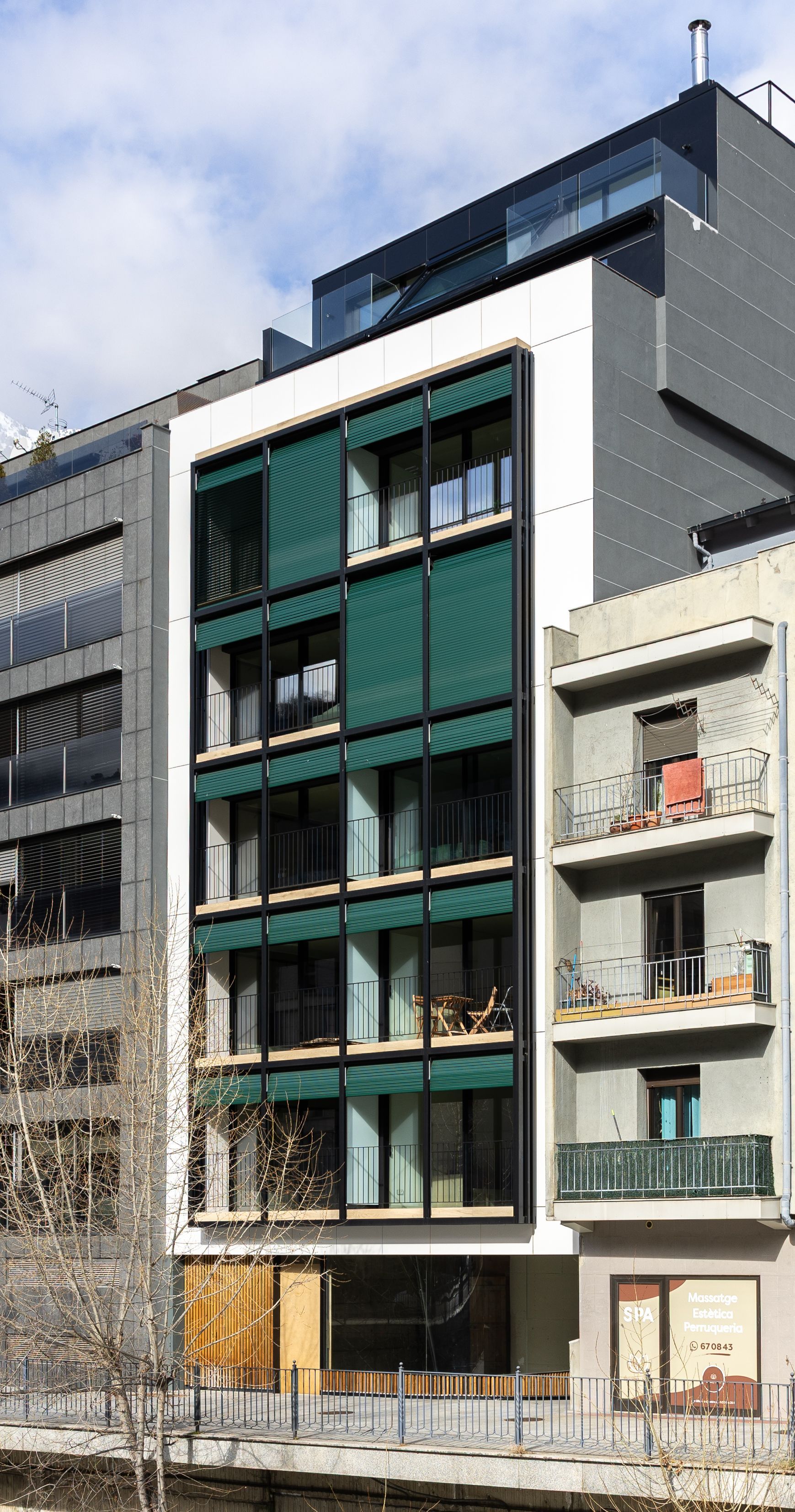 Edifici d'apartaments modern amb balcons verds i una façana grisa sota un cel ennuvolat
