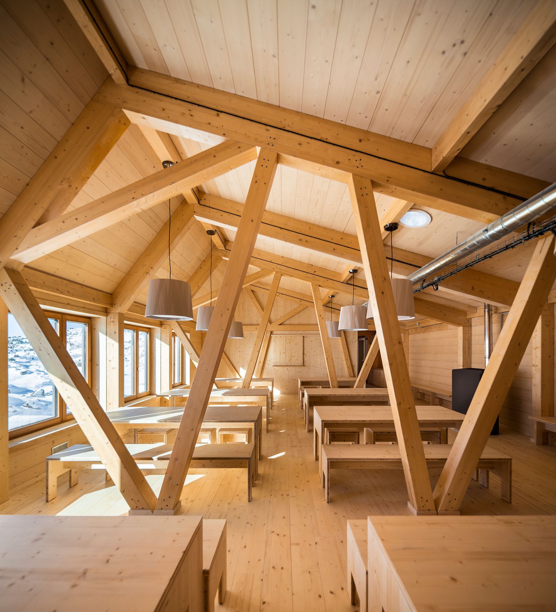 Interior de loft de fusta lluminós amb bigues a la vista, lliteres i sostre inclinat, il·luminat per grans finestrals