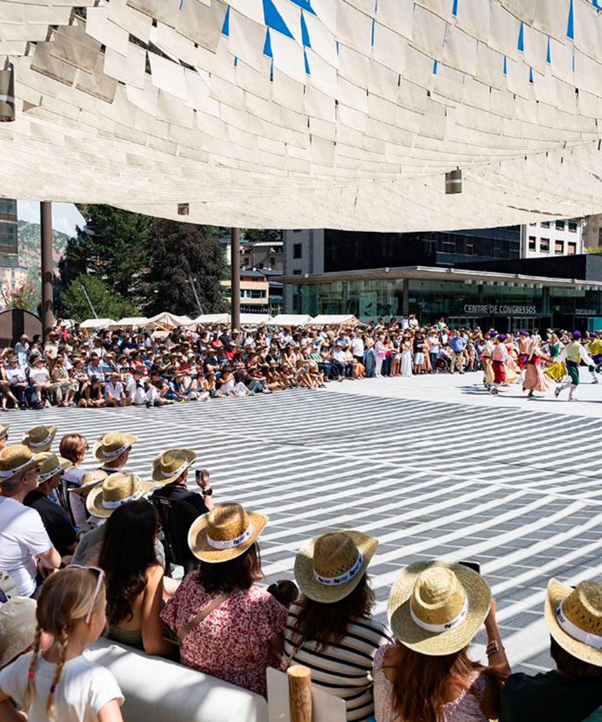 La multitud observa un espectacle de dansa colorit en una plaça assolellada sota una gran marquesina
