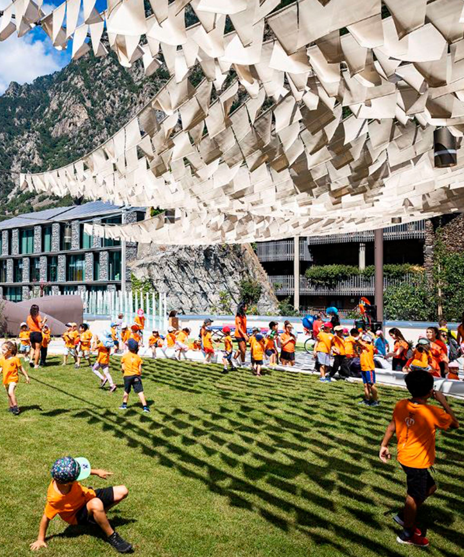 Nens jugant en un camp d'herba sota una marquesina blanca al costat d'un edifici modern.