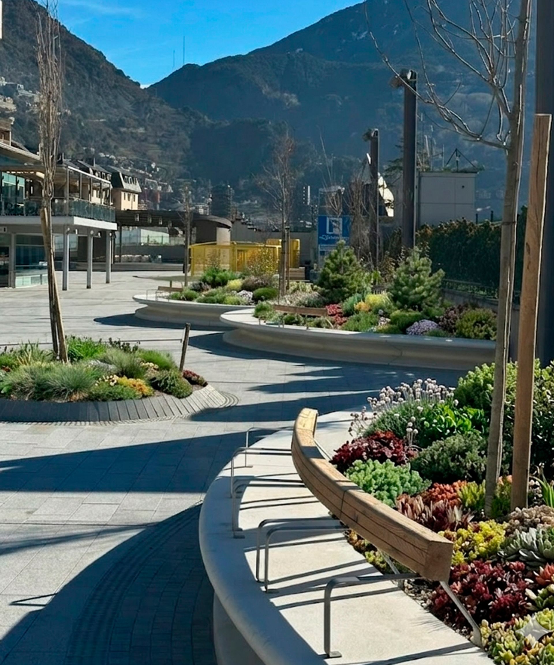 Passeig paisatgístic corbat amb parterres de flors i muntanyes al fons en un dia assolellat