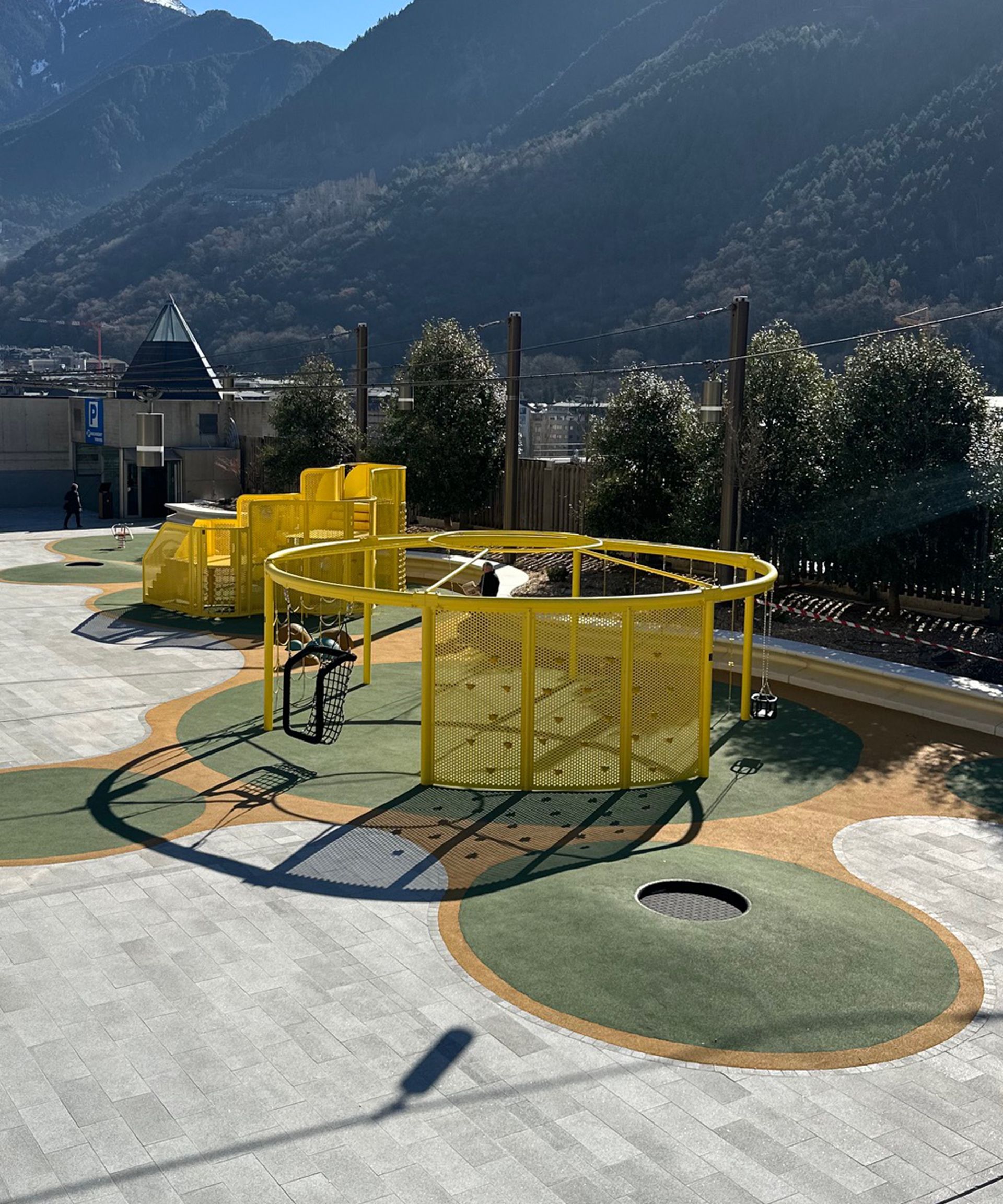 Equipament de joc groc en una pista de formigó amb muntanyes al fons
