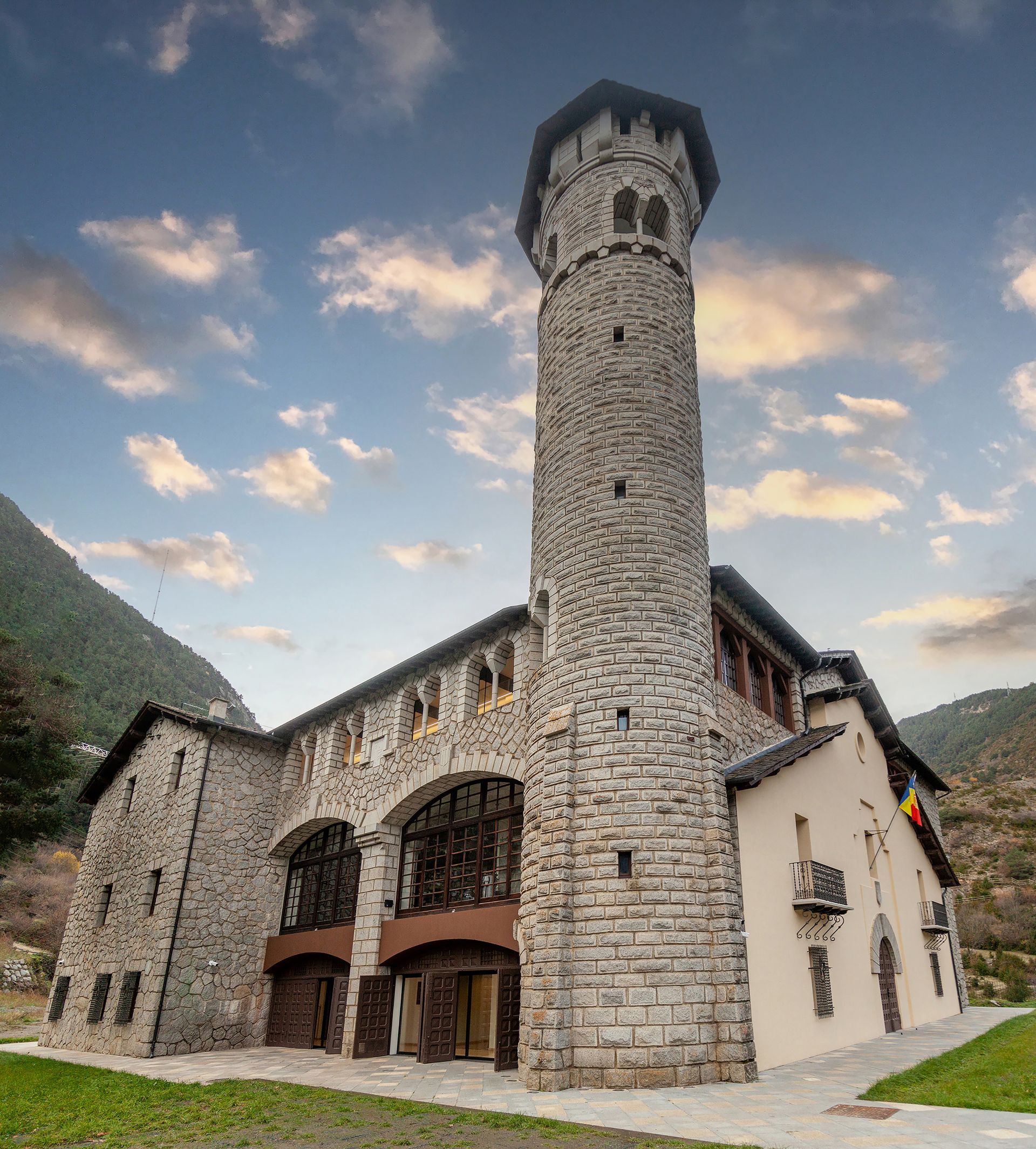 Església de pedra amb una torre rodona alta i portes de fusta amb arc, situada en una vall de muntanya al capvespre