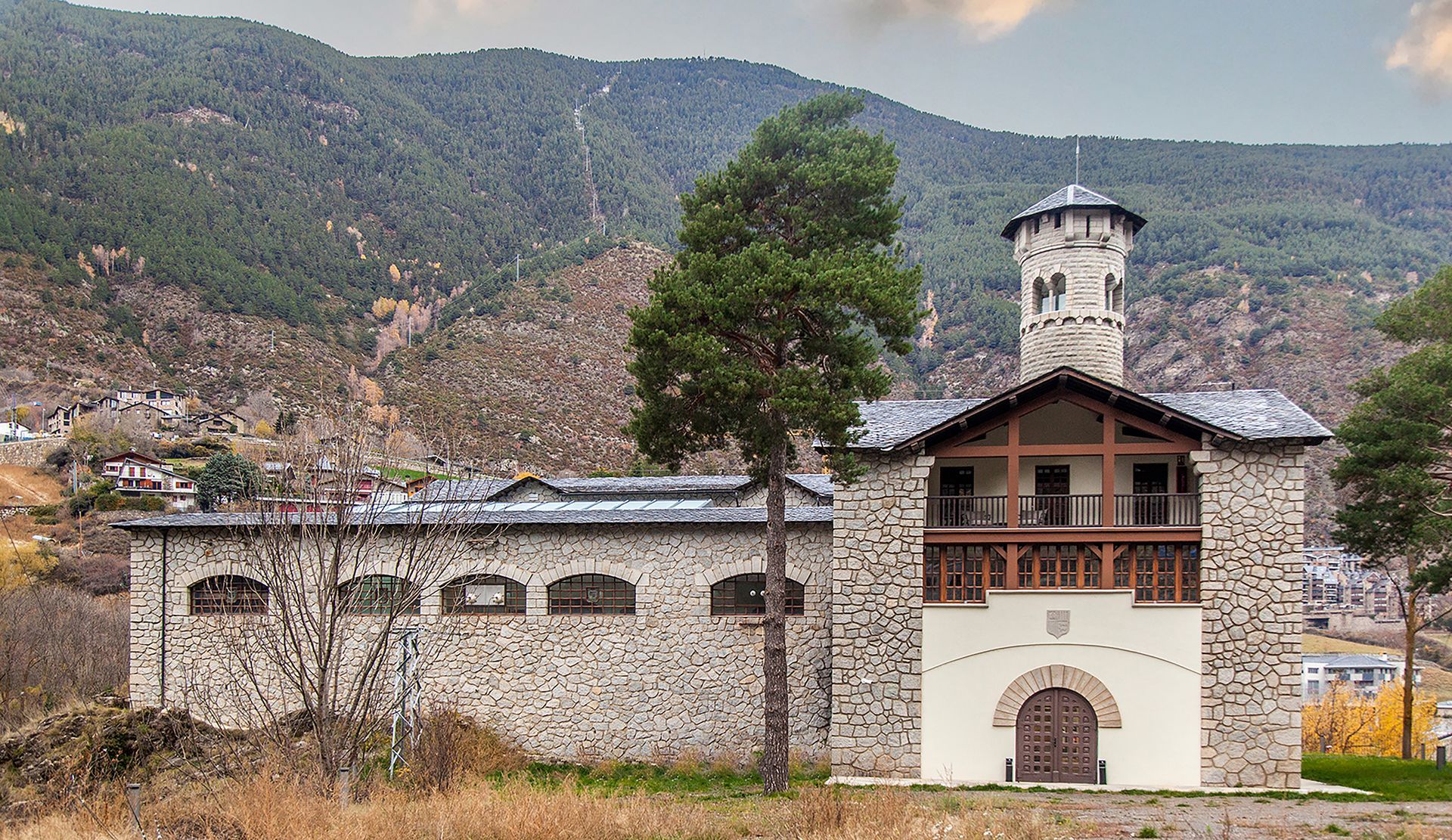 Església de pedra amb campanar i entrada amb arc en un poble de muntanya, envoltat de turons boscosos