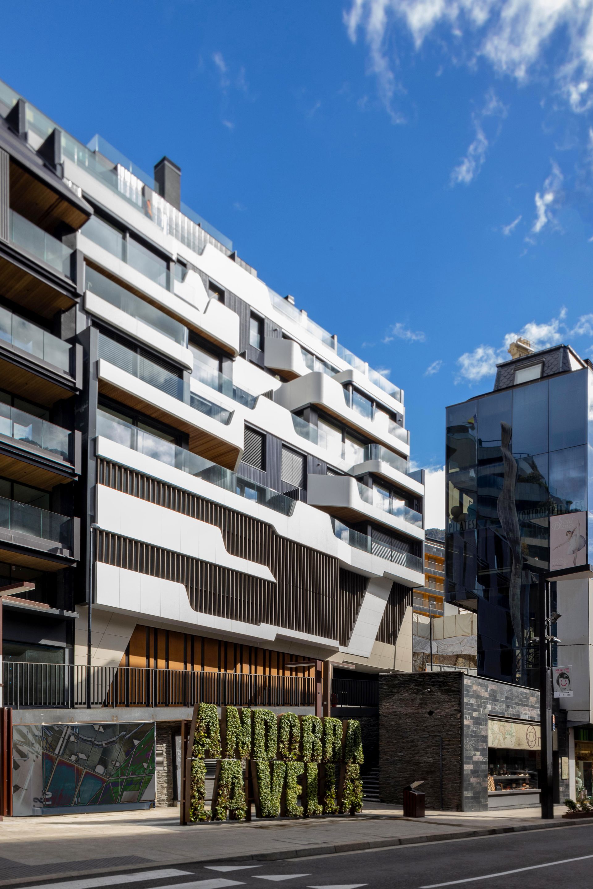 Edifici d'apartaments blanc modern amb balcons al costat d'una paret de pedra sota un cel blau brillant