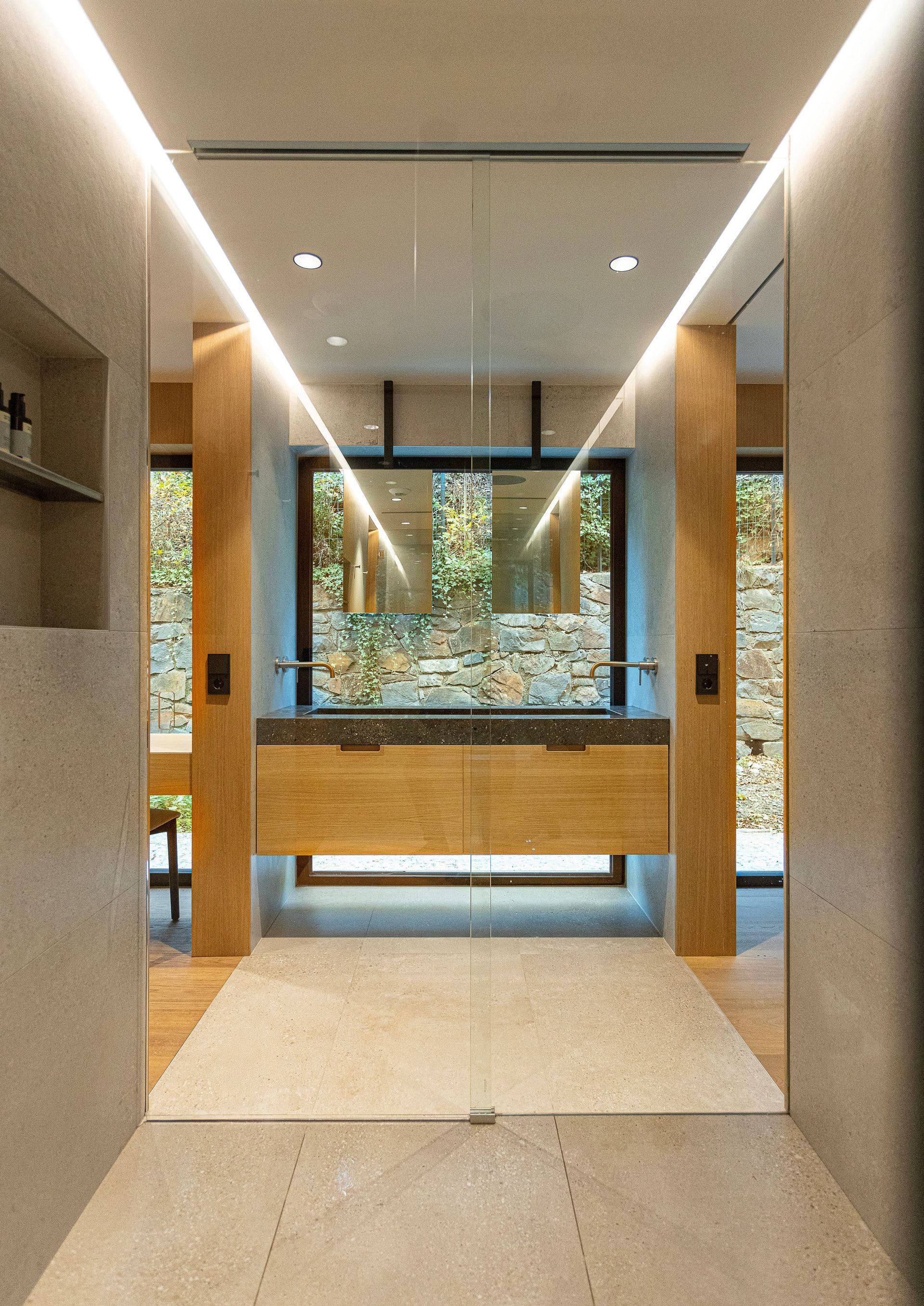 Passadís modern amb detalls de fusta, il·luminació encastada i una obertura de vidre a una vista exterior verda