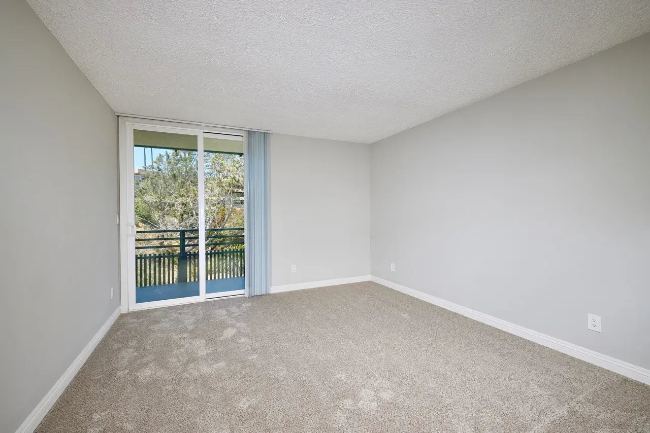 Empty bedroom with carpet and sliding glass door leading to a balcony.
