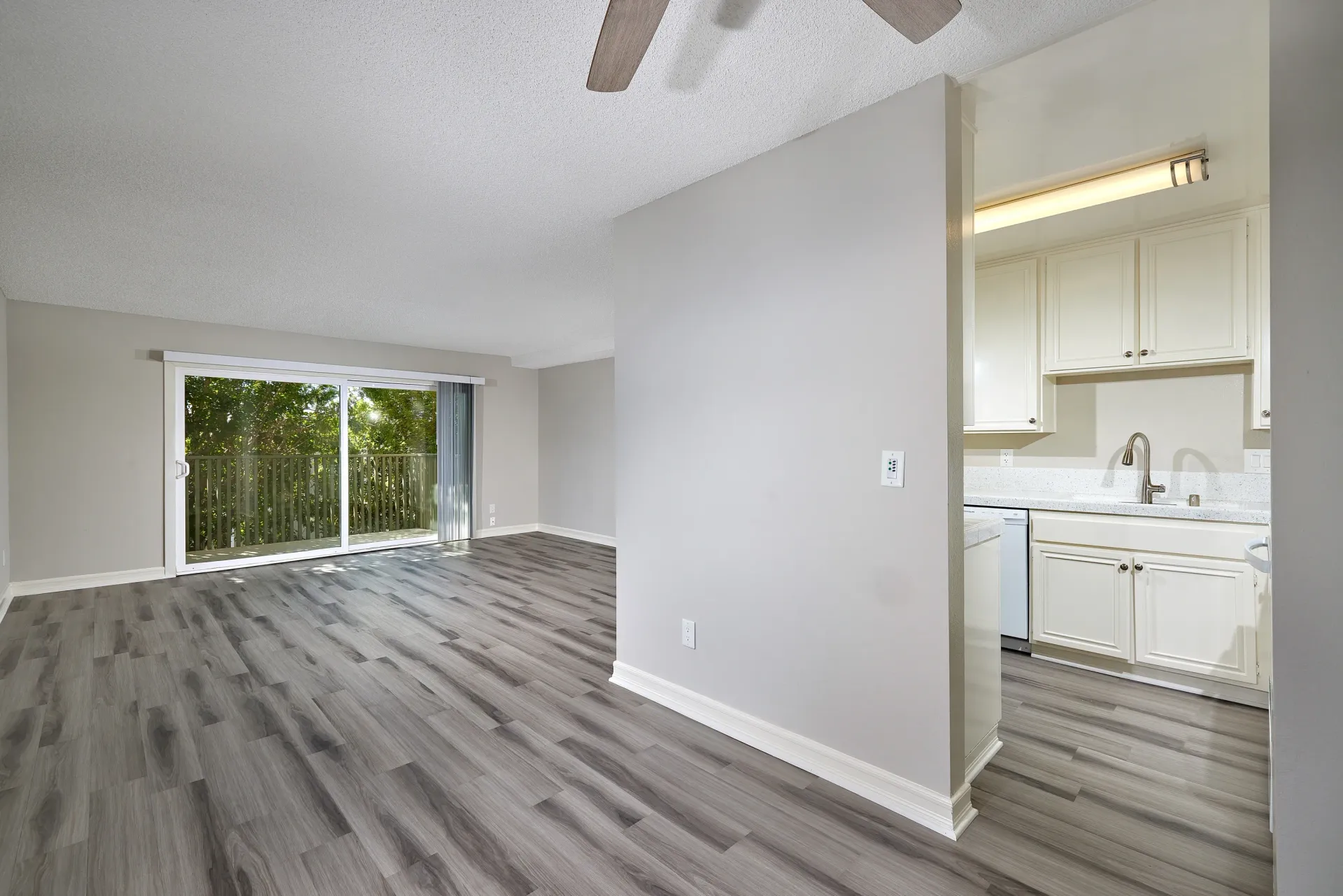 Living room and kitchen of an apartment with wood plank flooring and sliding glass door.
