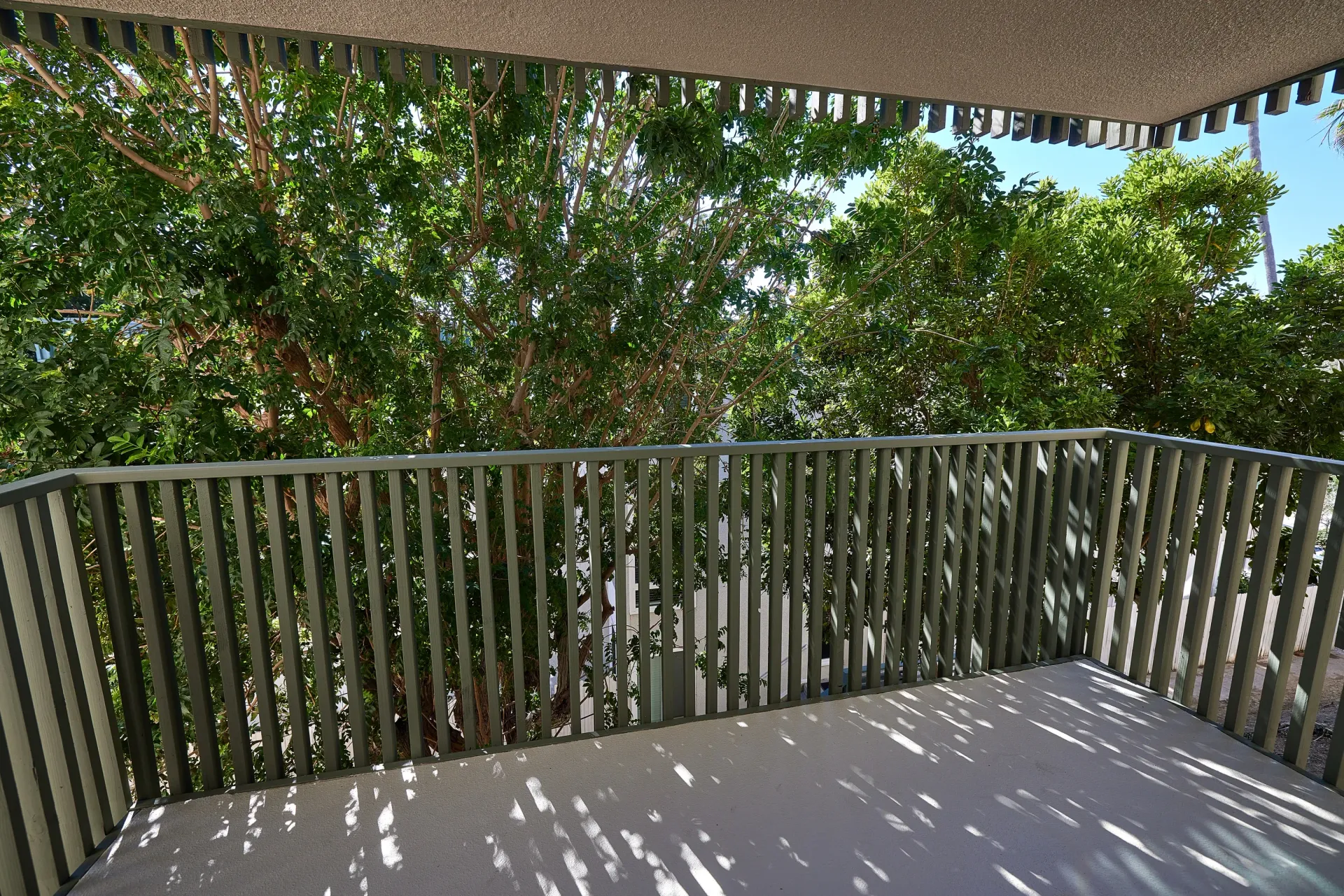 Balcony view with lush green trees and sunlight filtering through the railing.