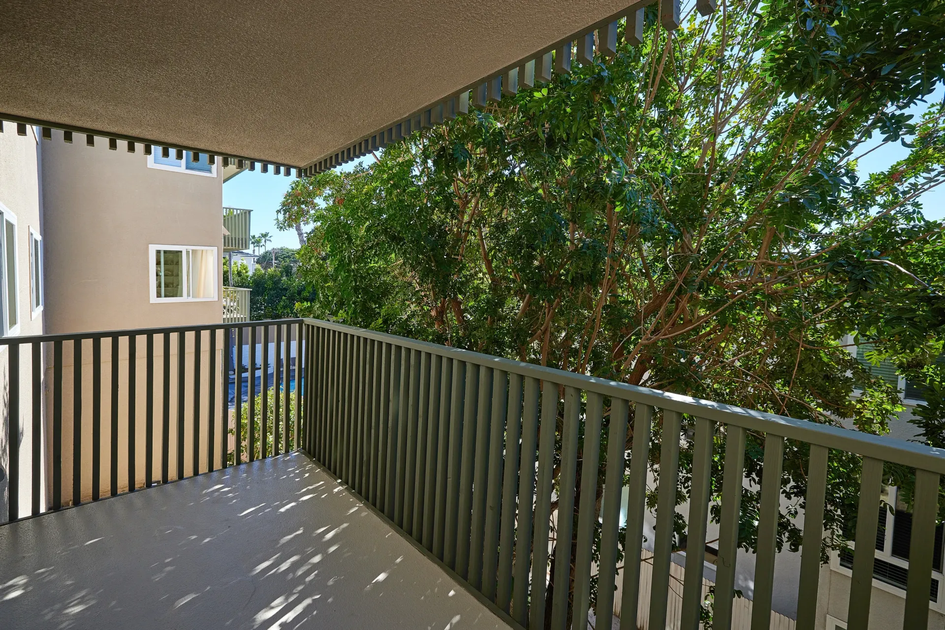 Balcony with a view of trees and a pool.