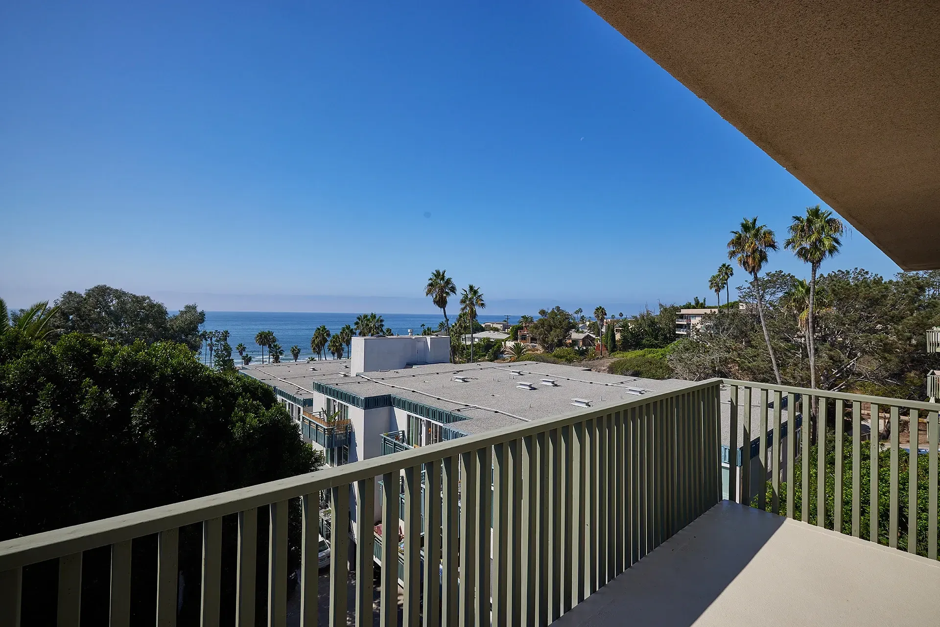 View from balcony overlooking buildings and the ocean with palm trees.
