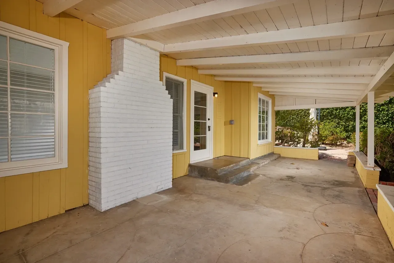 Covered patio with a white brick fireplace, yellow siding, and a white ceiling.