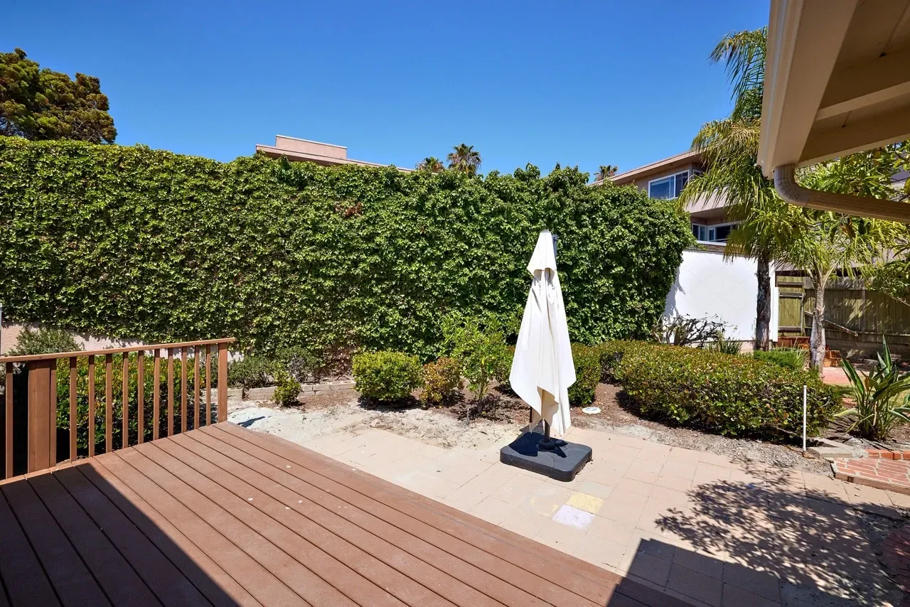 Patio with a white umbrella and a wooden deck, overlooking a wall covered in ivy.