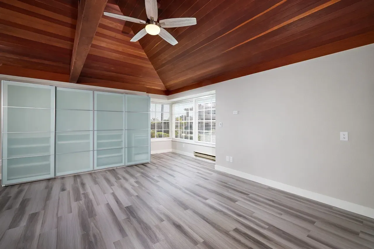 Spacious bedroom with vaulted wood ceilings, ceiling fan, and large frosted glass closet.
