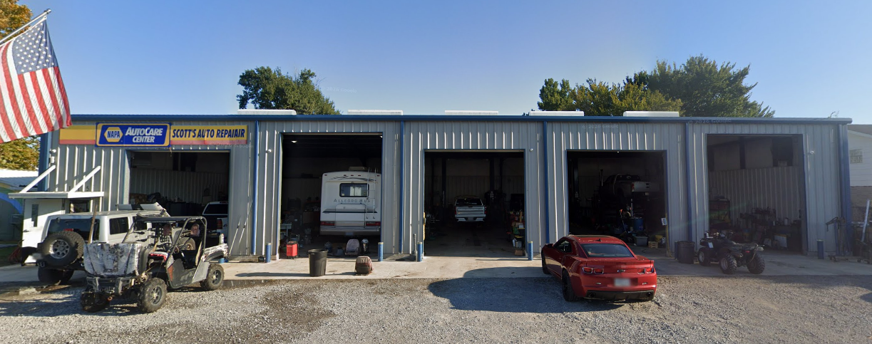 Auto repair garage with three open bays, parked ATV and red car, and a large American flag outside