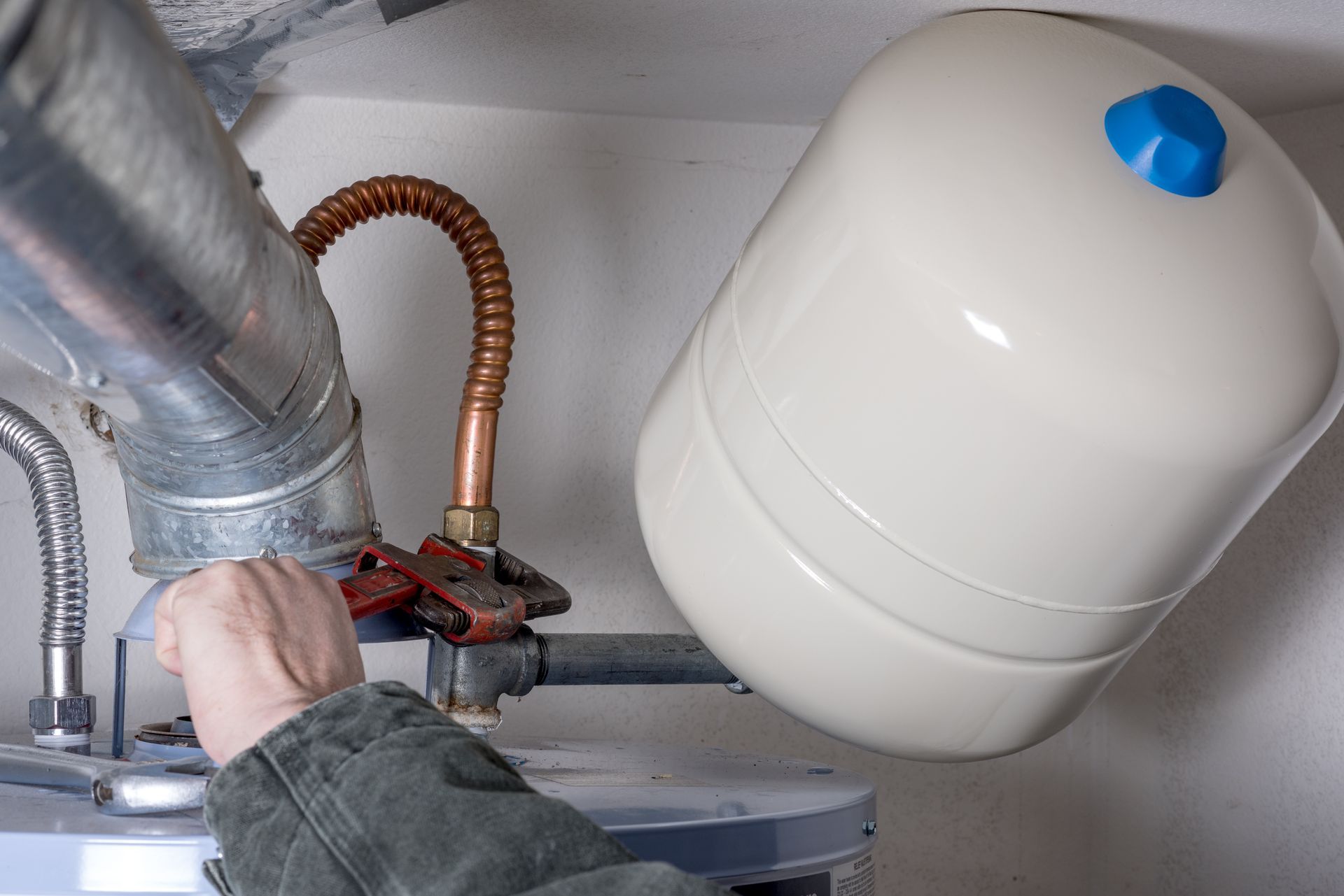 A person is fixing a water heater with a wrench.