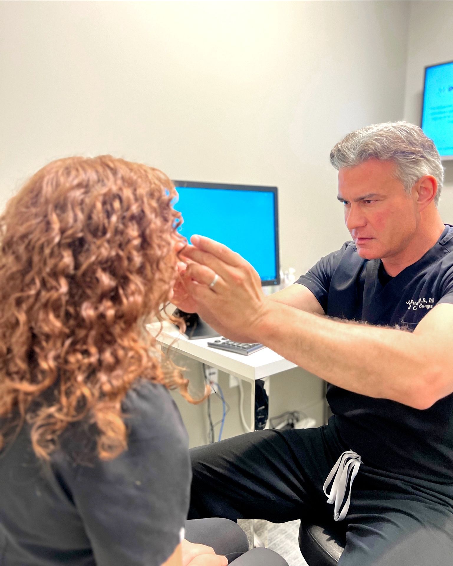 Doctor examining patient's ear in a medical office; doctor wears black scrubs, and patient has red curly hair.