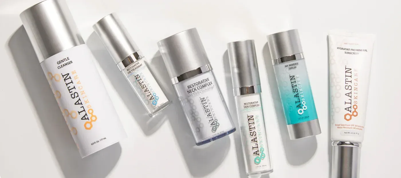 Skincare products with silver caps on a white surface. The brand name “ALASTIN” is visible on the bottles.