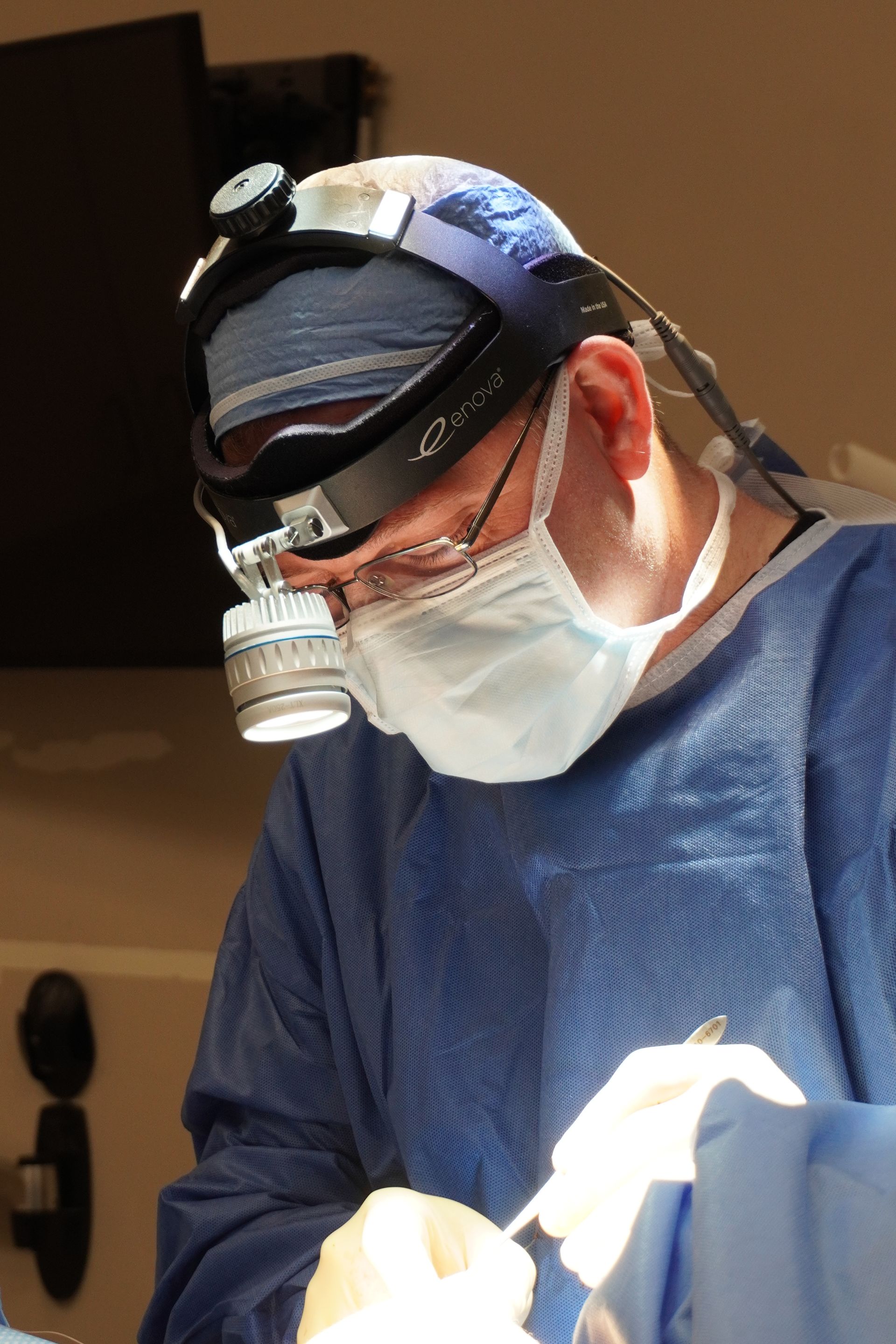 Surgeon in blue scrubs, mask, and headlamp, operating in a sterile environment.