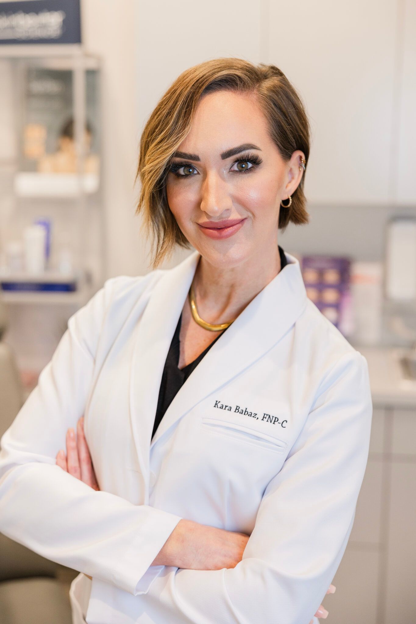 Woman in a white lab coat with arms crossed, smiling in a medical setting.