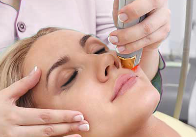Woman receiving laser skin treatment on her nose, close-up with therapist holding device.