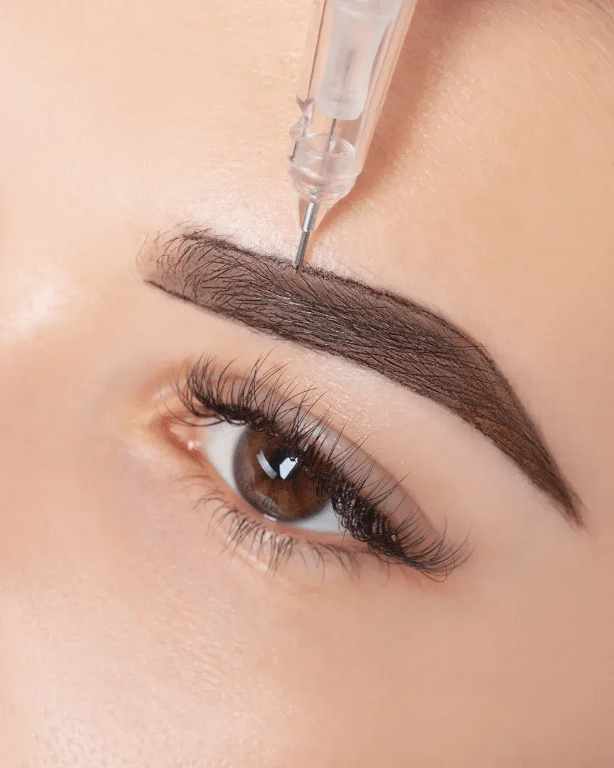 Eyebrow being tattooed with a needle. Close-up of eye, brow filled with dark pigment.