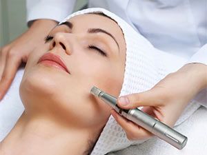 Woman receiving a microneedling treatment on her face. A gloved hand uses a device on her cheek.