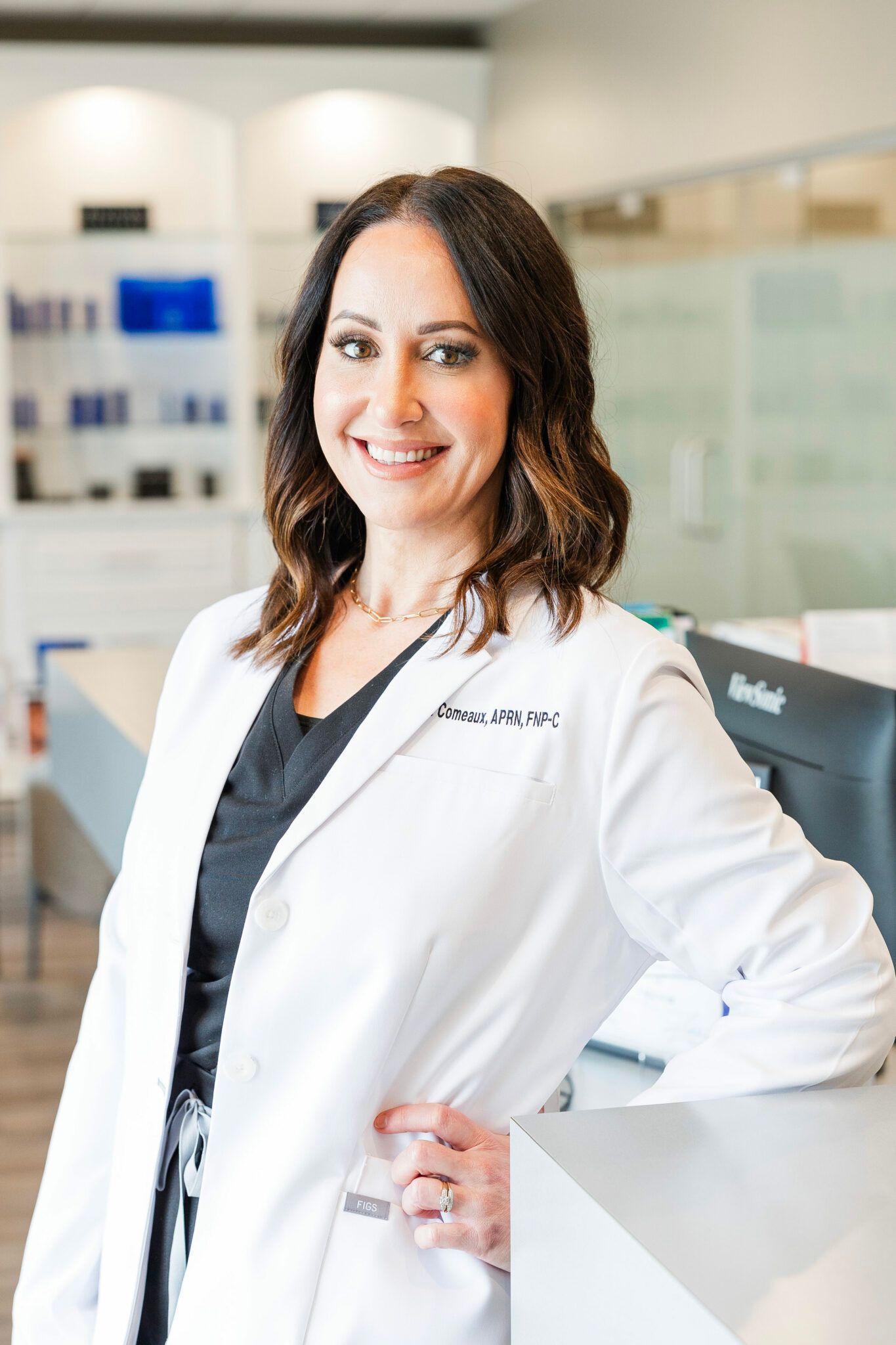 Woman in white lab coat smiles, leaning on counter, office setting.