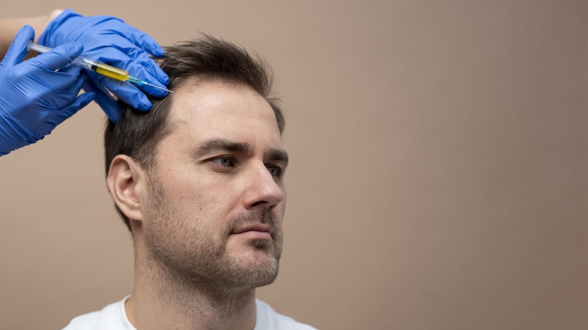 Person receiving an injection in their scalp; blue gloves and a syringe.