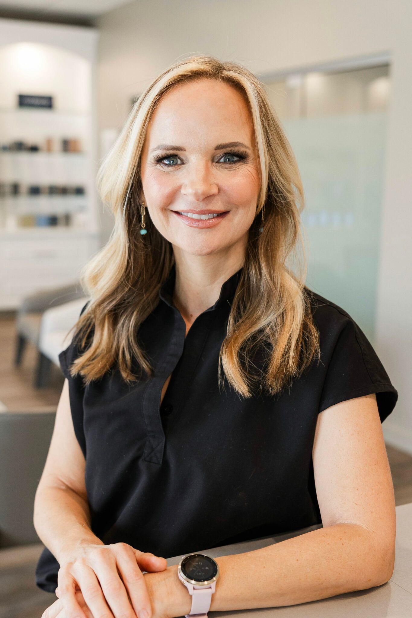 Woman with blonde hair wearing a black shirt, smiling, arms crossed on a counter in a modern office.