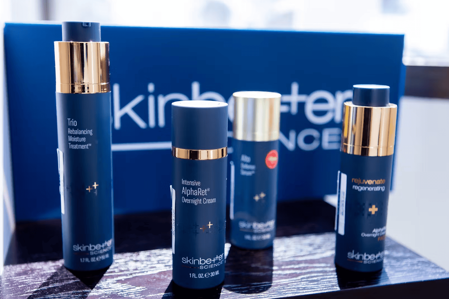 Four dark blue skincare product bottles with gold accents on a display table.