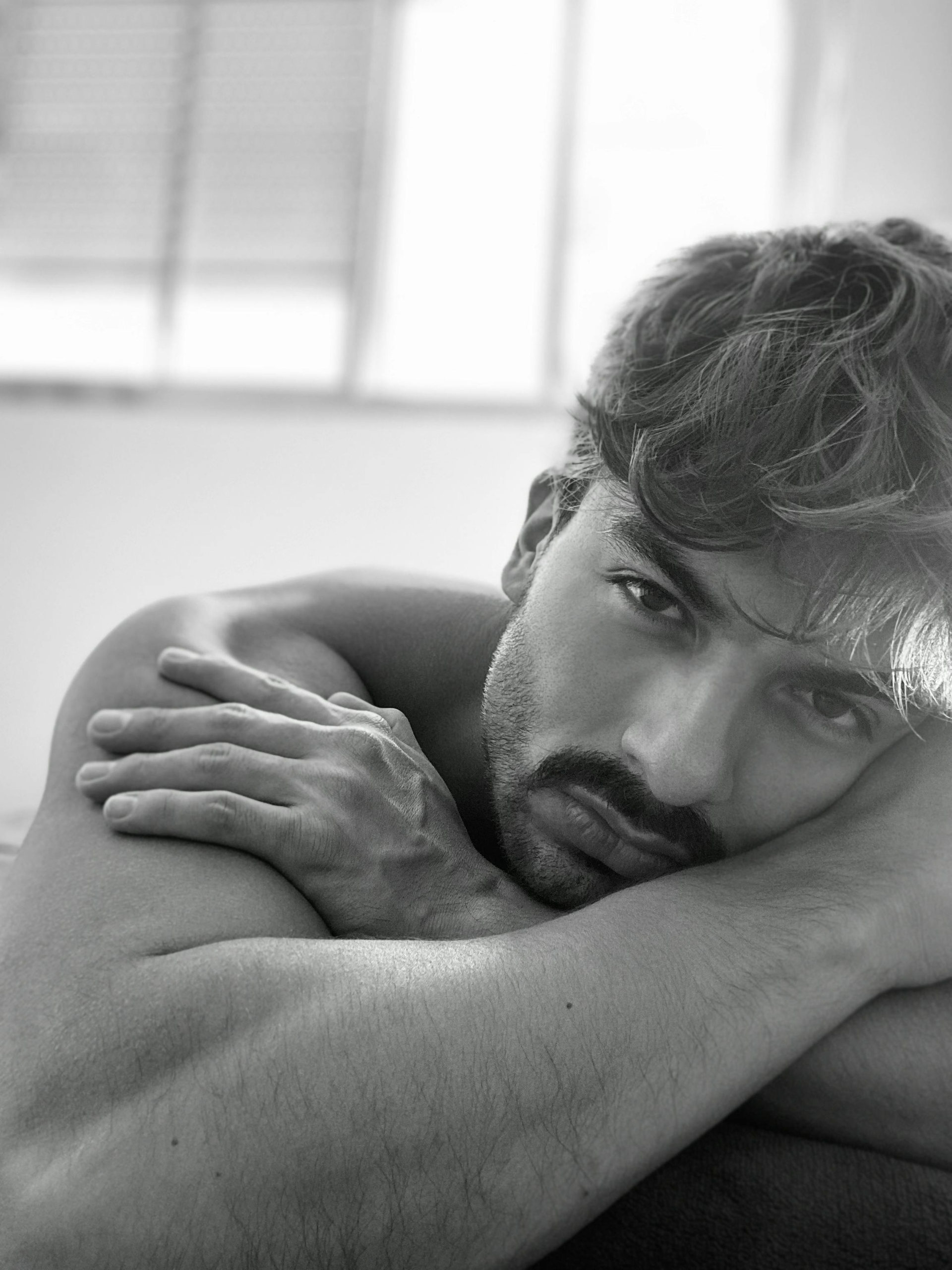 Man with short, wavy hair, resting his head on arms, looking at the camera. Black and white.
