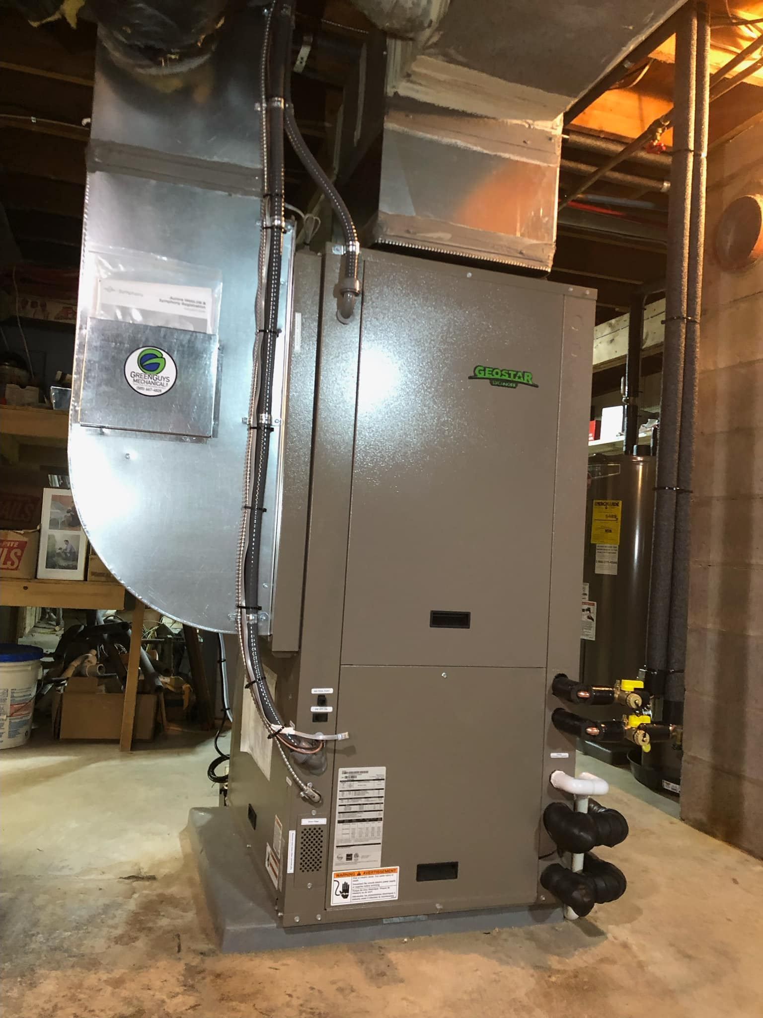 Interior view of a grey geothermal heating and cooling HVAC unit with ductwork in a residential basement.
