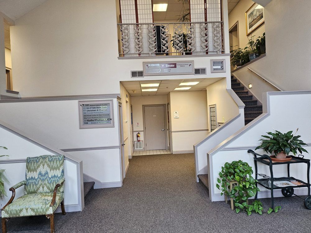Bright office lobby with stairs, balcony, hallway, and a chair by a potted plant