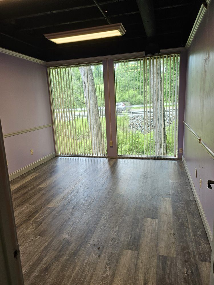 Empty room with wood flooring, pink walls, and large glass doors with vertical blinds.