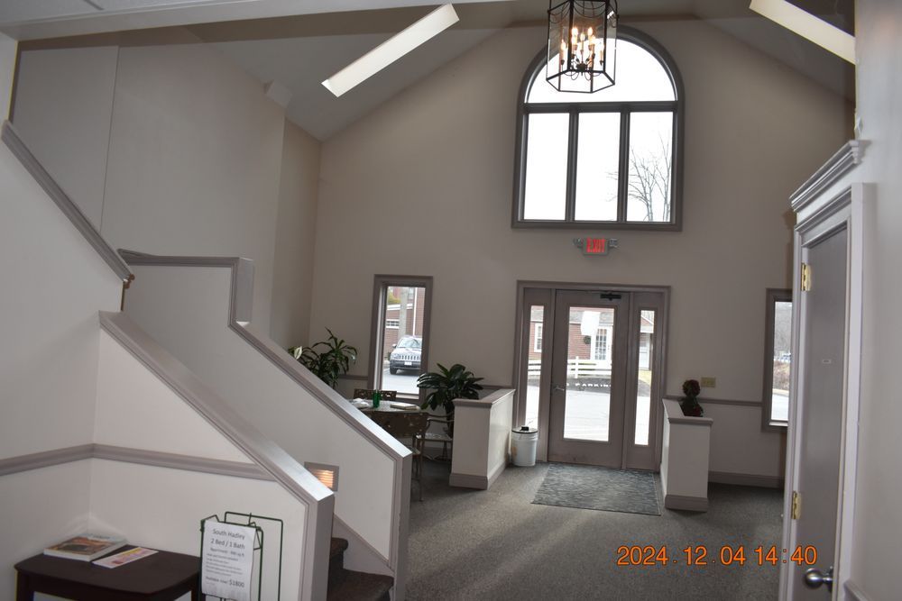 Bright lobby with staircase, arched window, glass entrance doors, and white walls