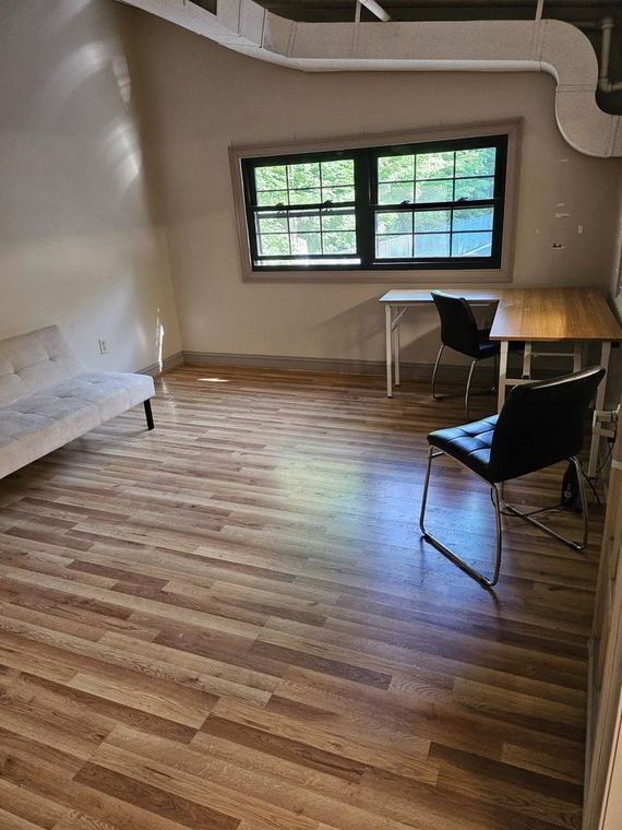 Empty room with wood floors, curved white wall, large window, and a table with chairs.