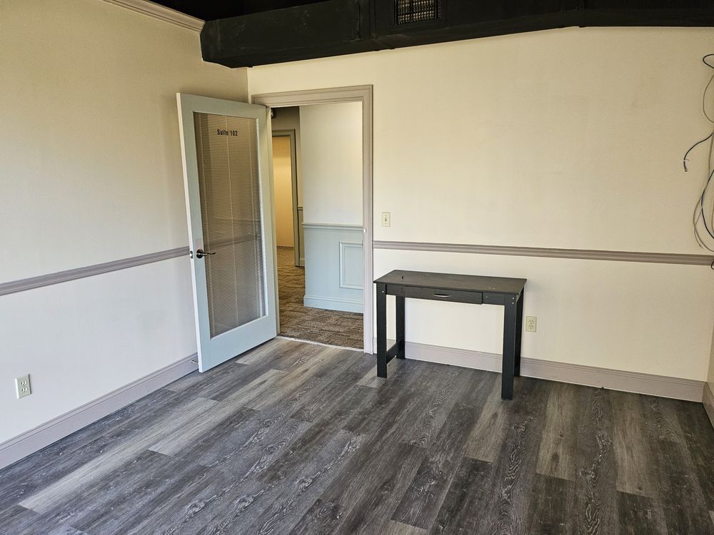 Empty room with gray wood floor, white walls, open door, and small black table.