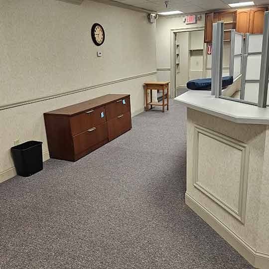 Empty office hallway with a wall clock, cabinet, trash bin, and a reception counter.