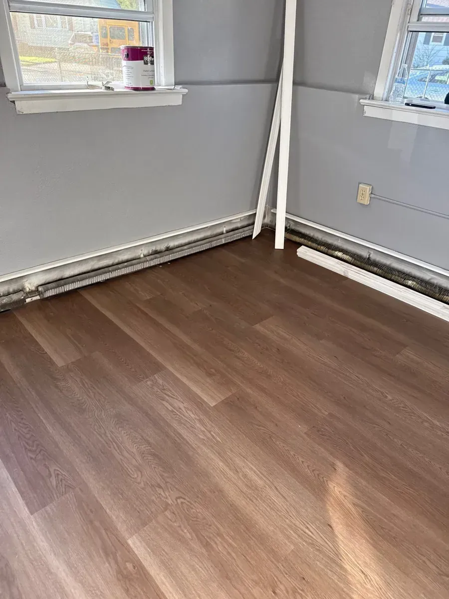 Same corner of the Piscataway, NJ room restored with new plank flooring and white baseboard