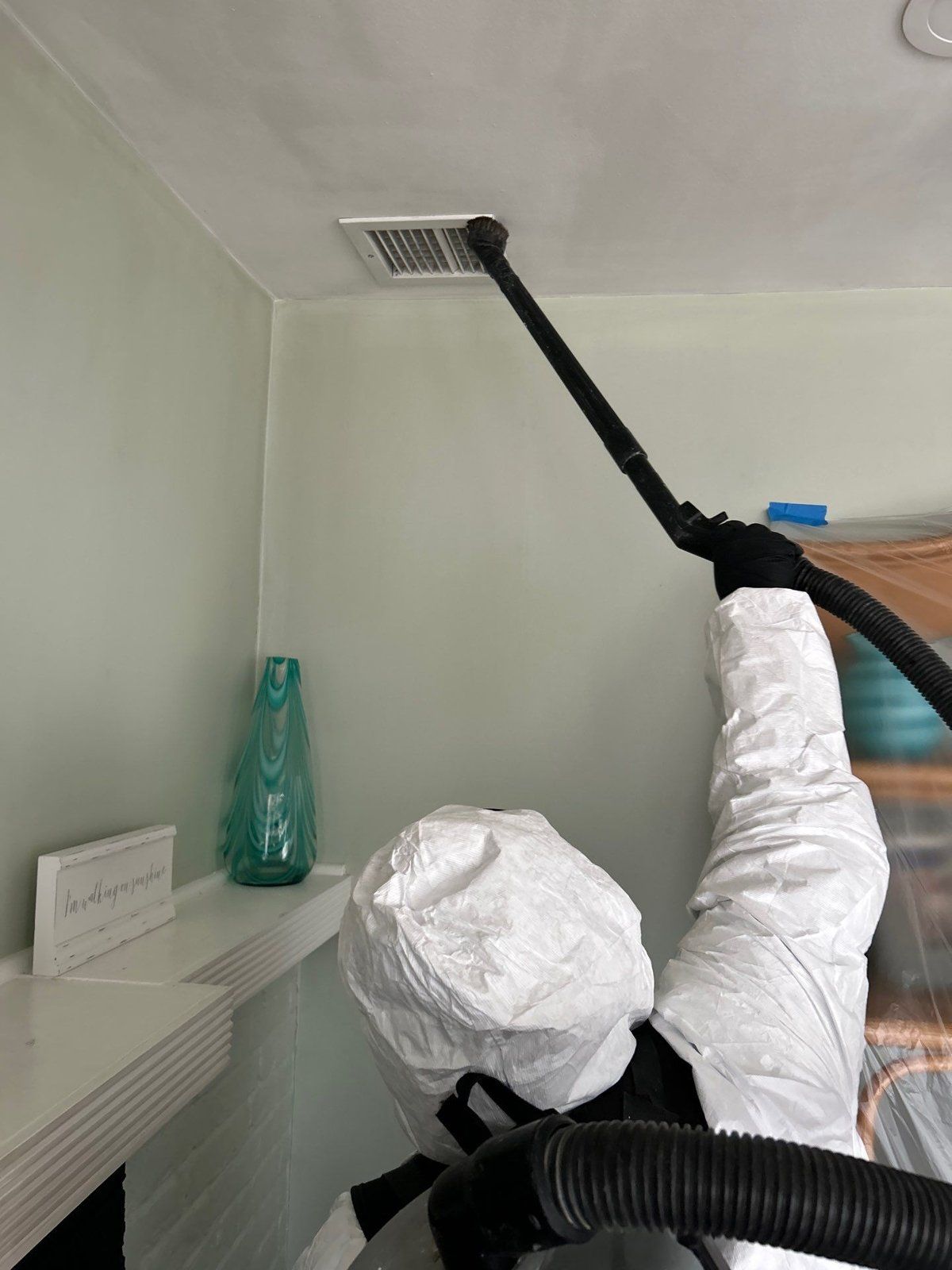 Technician in protective suit HEPA-vacuuming soot from a ceiling supply vent