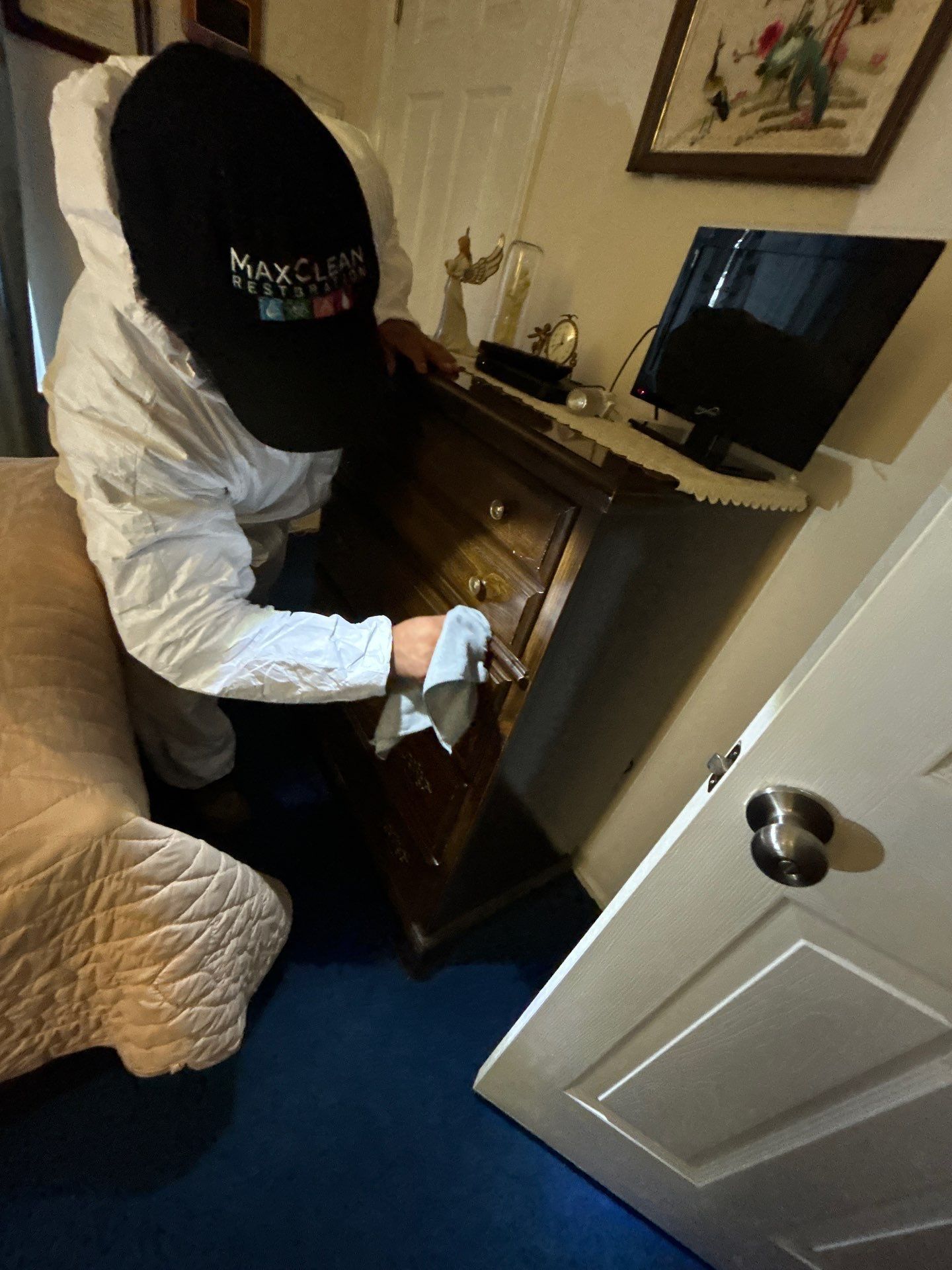 Restoration technician in branded protective gear cleaning soot from a dresser after a furnace puff-back