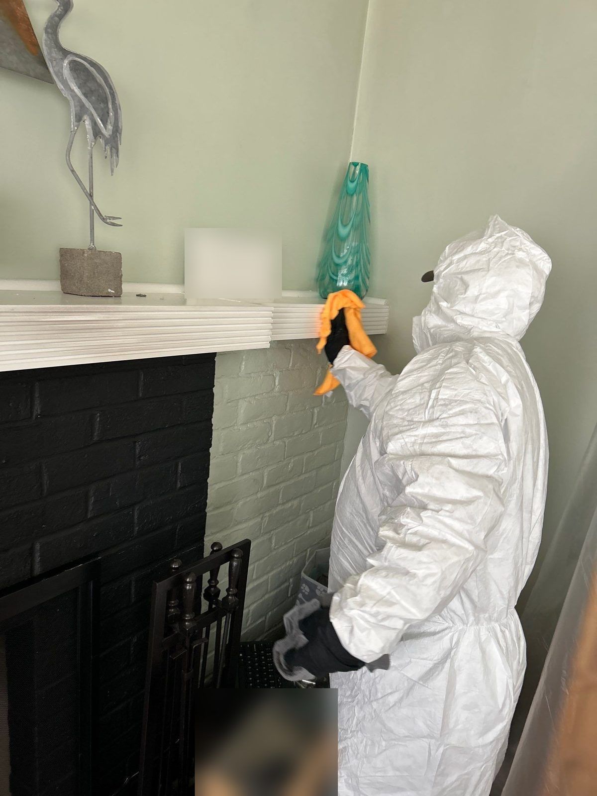 Technician in a protective suit wiping smoke residue from a fireplace mantel and decor