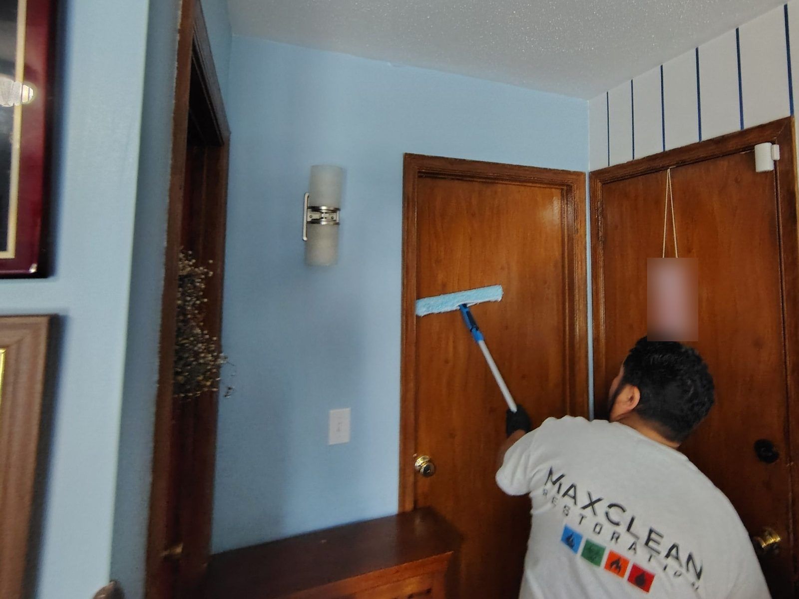MaxClean technician washing smoke residue from walls and doors with a pole sponge after a fire