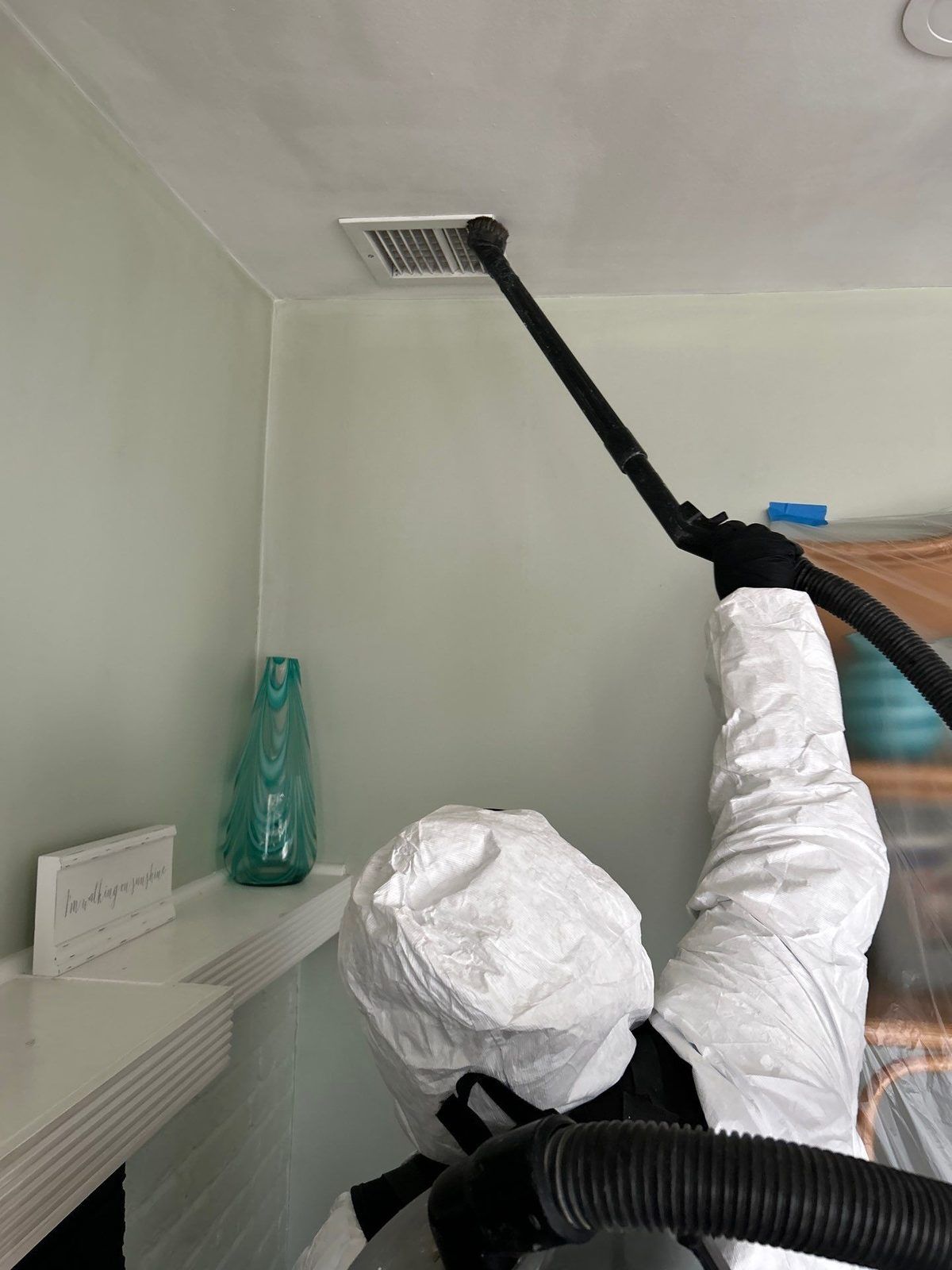 Technician HEPA-vacuuming a ceiling vent after a furnace puff-back