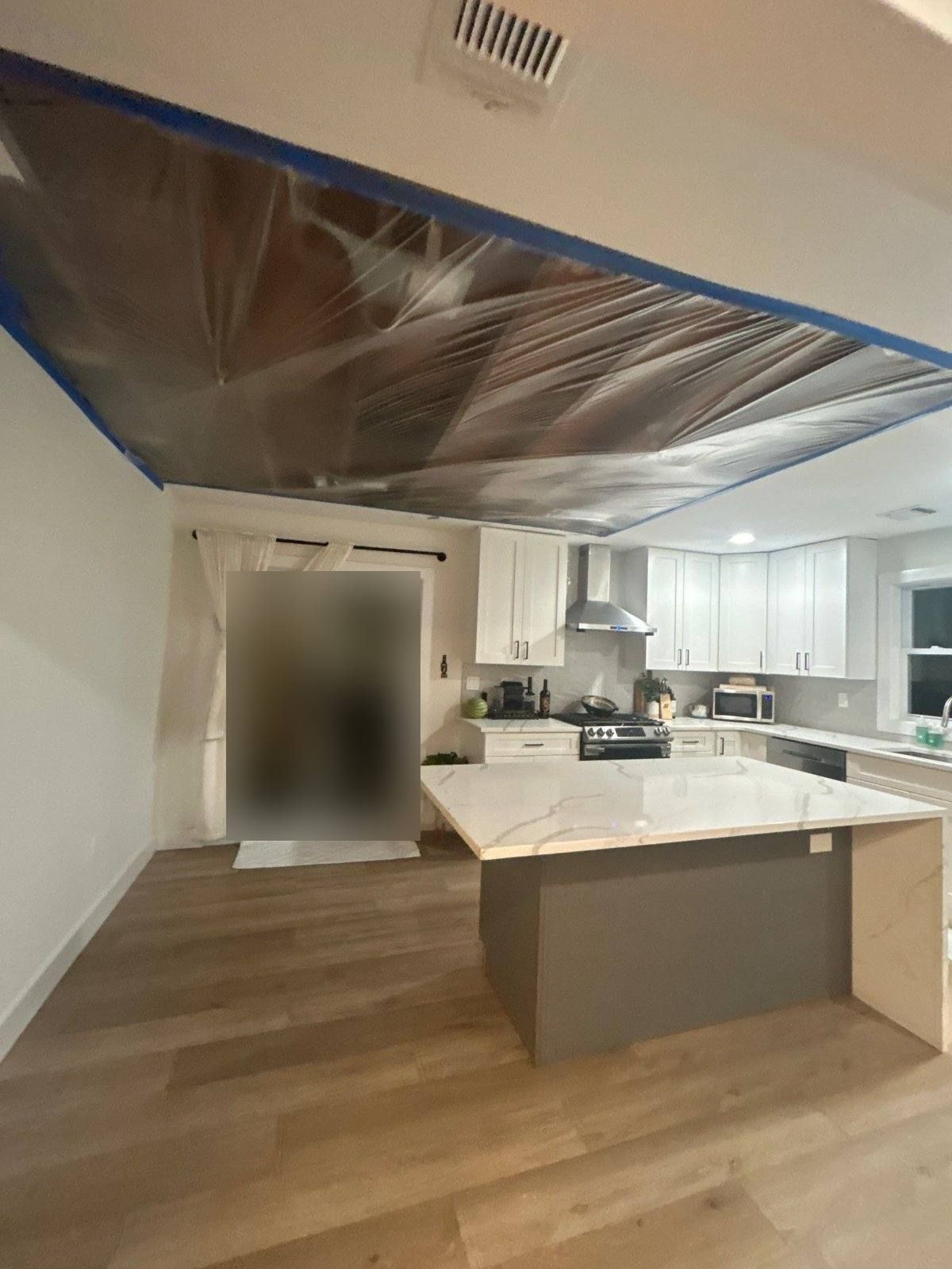 Kitchen ceiling opened and covered in plastic sheeting with blue tape during water damage drying