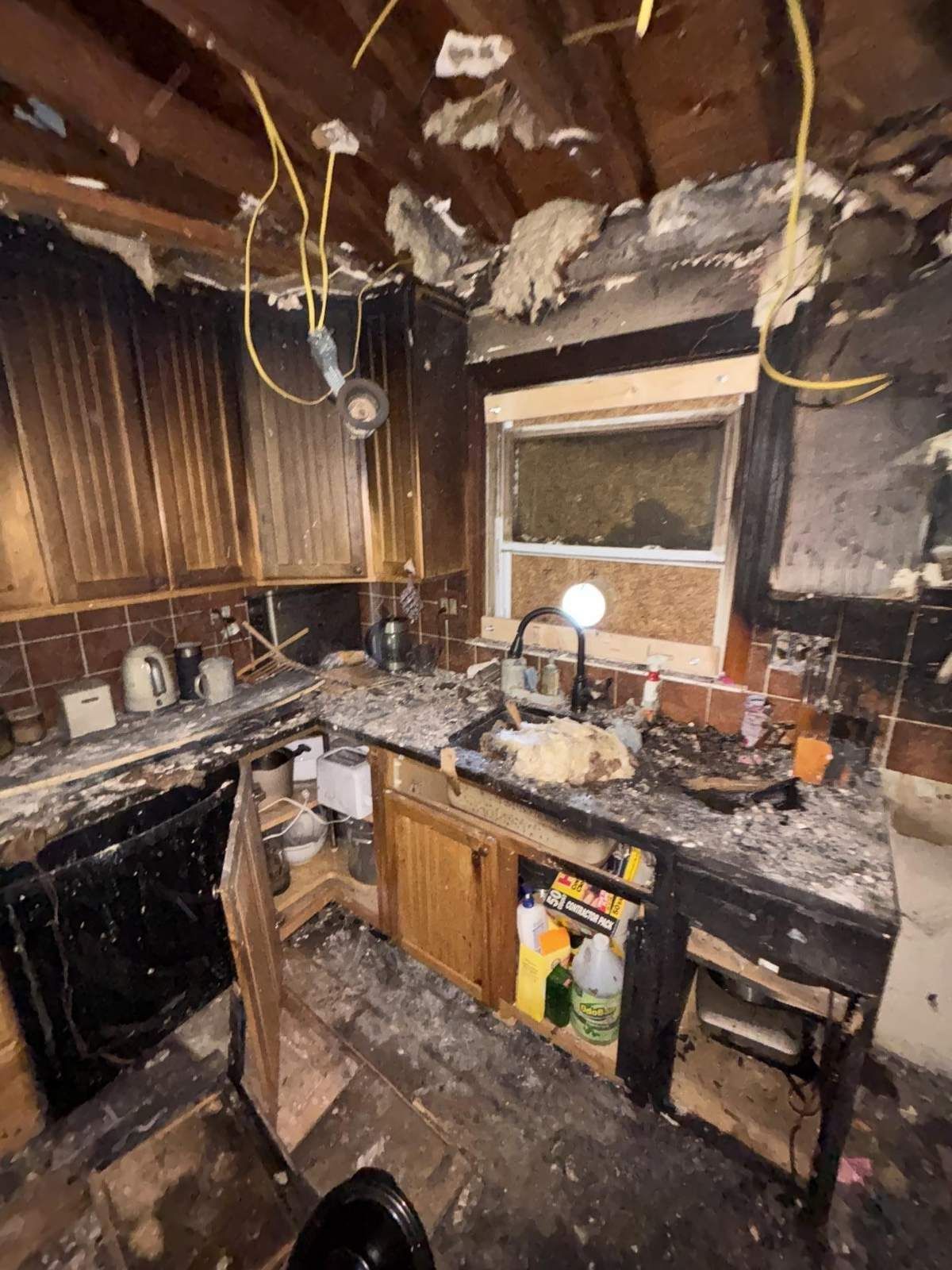 Fire-damaged kitchen with soot-covered cabinets, ash on counters and an opened ceiling