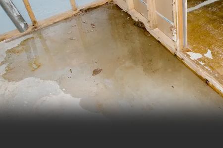 Water pooling on a concrete floor near a wooden frame, appearing dirty and damaged.