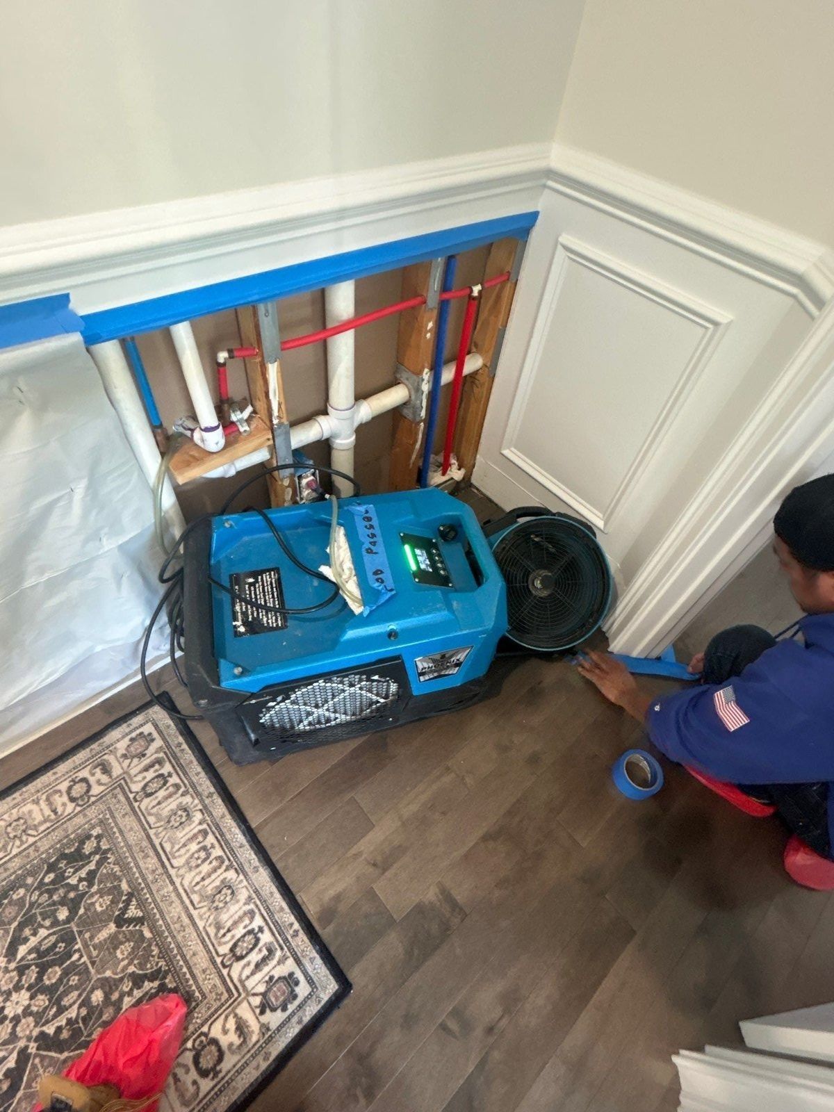 Technician setting up a dehumidifier and air mover by an opened wall with exposed water pipes